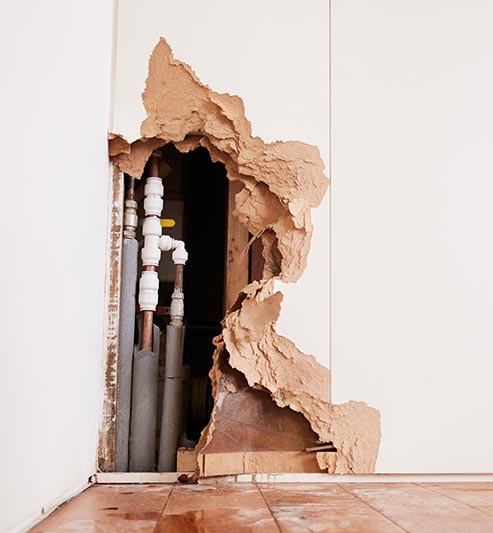 A hole in a building wall next to plumbing due to water damage that could be prevented with commercial water leak detection.