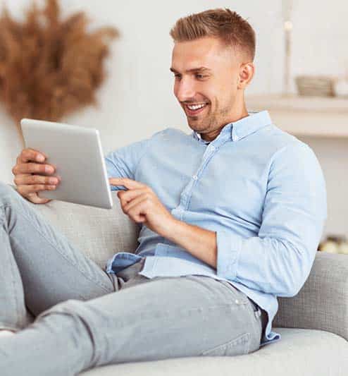 Guy sitting on couch using tablet app to control his home thermostat