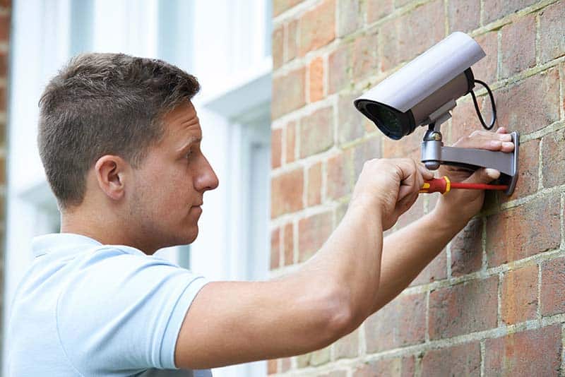 a technician installs a security camera to an exterior brick wall for optimal placement